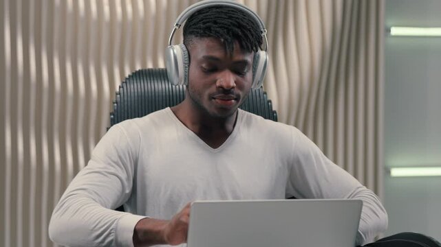African American man put on headphones open laptop start working day gaming in futuristic service using modern futurism innovation technology guy male putting on earphones typing computer indoors