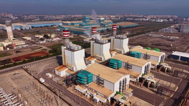 Aerial view of combined cycle gas turbine power plant with HRSG units, exhaust stacks, cooling systems and high-voltage substation feeding grid infrastructure