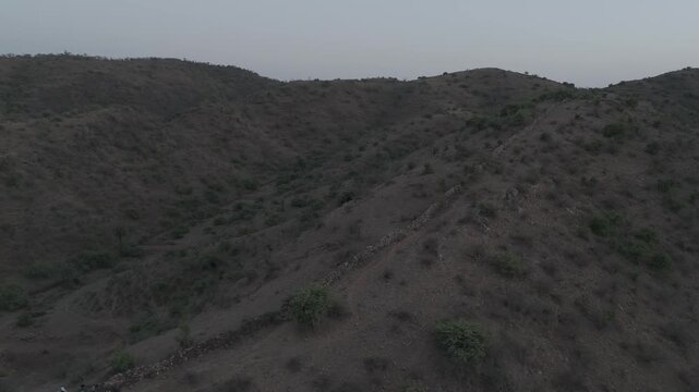 Aerial view of the Aravalli hills near Udaipur, Rajasthan during spring evening, showing rugged terrain with native trees like palash, semal, and rohida across the landscape.