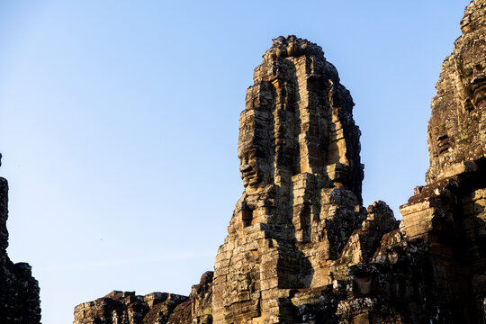 View of the ancient stone faces of Bayon Temple rise majestically under a clear sky, their weathered surfaces whispering tales of centuries past, Siem Reap, Cambodia.
