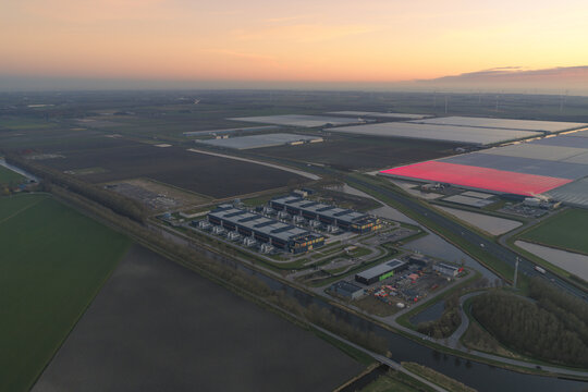 Aerial view of the data center contrasting with green fields and a red solar field under a fading sunset sky, Middenmeer, North Holland, Netherlands.