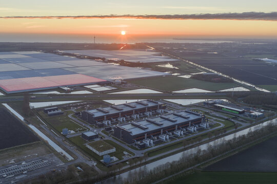 Aerial view of a sprawling industrial complex bathed in the warm glow of the setting sun with a play of light and shadow, Middenmeer, North Holland, Netherlands.
