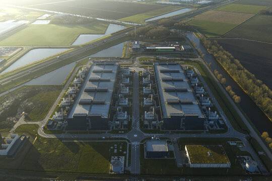 Aerial view of the expansive data center complex, its geometric shapes juxtaposed against the soft, diffused light of early morning, Middenmeer, North Holland, Netherlands.