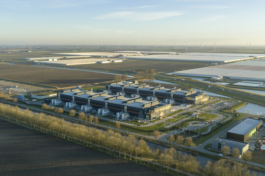 Aerial view of vast data centers sprawling across the flat landscape, reflecting the pale sky, with canals cutting through the fields, Middenmeer, North Holland, Netherlands.