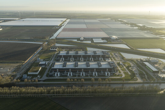 Aerial view of geometric fields and modern industrial architecture meet the horizon under the diffused light, creating a tapestry of human endeavor, Middenmeer, North Holland, Netherlands.