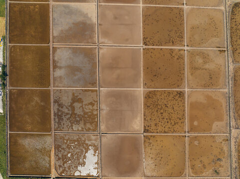 Aerial view of a geometric tapestry of salt ponds reflecting the sky, creating a mosaic of earthy browns and shimmering whites, Ston, Dubrovnik-Neretva County, Croatia.