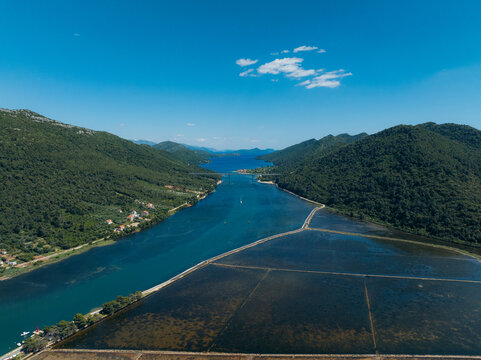 Aerial view of the shimmering, turquoise waters snaking through verdant hills alongside the geometric patterns of the salt pans, Ston, Dubrovnik-Neretva County, Croatia.