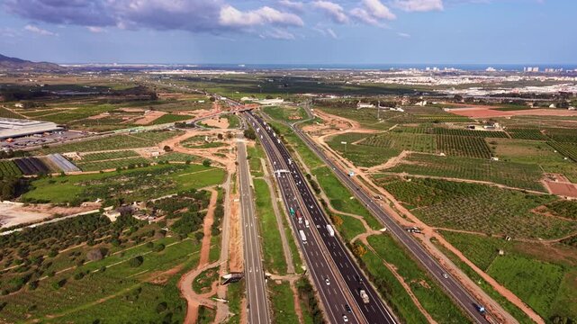 Aerial view of multi-lane highway corridor in Moncada with grade-separated interchange, service roads, traffic flow, drainage channels and agricultural parcels in Valencia region