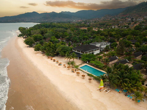 Aerial view of Tokeh Beach featuring a resort with a swimming pool, palm trees, and white sand against a backdrop of lush mountains in Western Area Rural, Western Area, Sierra Leone.