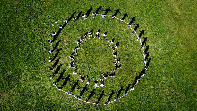 Aerial view of children in concentric circles on bright green grass cast long shadows in the sunlight, Bogeve, Auvergne-Rhone-Alpes, France.