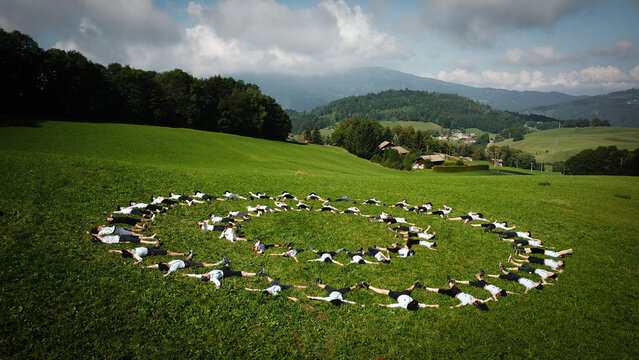 Aerial view of people lying on the grass in a spiral pattern under a bright sky, Bogeve, Auvergne-Rhone-Alpes, France.