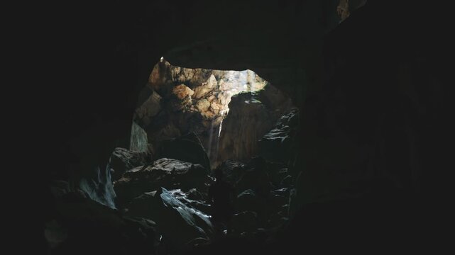Handheld footage of underground cave with sunlight ray illuminating rock formations and jungle plants in Laos, Southeast Asia