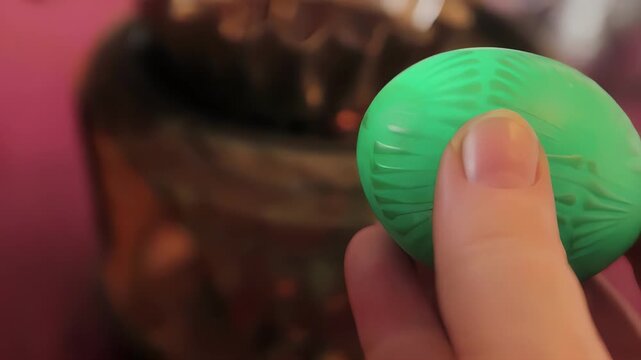 Close-up of a hand holding a green decorative Easter egg with intricate patterns