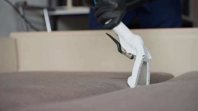 Caucasian Specialist Steam Extracting Sofa Fabric, White Extractor Nozzle And Hose Pulling Embedded Stain, Focused Upholstery Cleaning And Stain Removal, Gloved Technician At Work