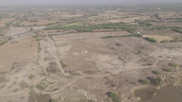 Aerial view of agricultural fields in Bhilwara, Rajasthan during spring harvest season, showing green, yellow, and dry crop patterns with scattered native trees across rural farmland.