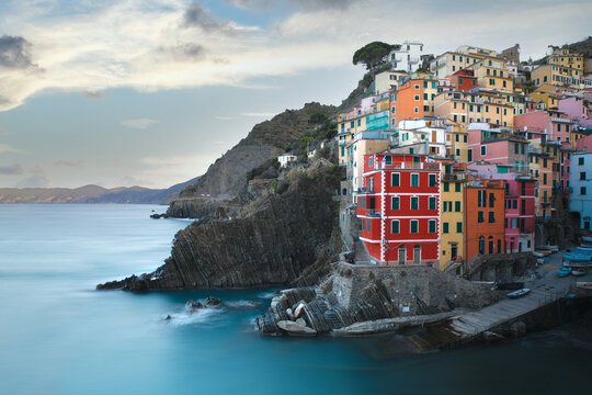 Aerial view of colorful houses perched on a rocky cliff overlooking the turquoise sea in Riomaggiore, Liguria, Italy.