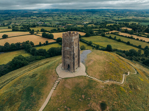 Aerial view of the iconic Glastonbury Tor piercing the sky, a stark contrast to the soft, undulating Somerset Levels below, Glastonbury, England, United Kingdom.