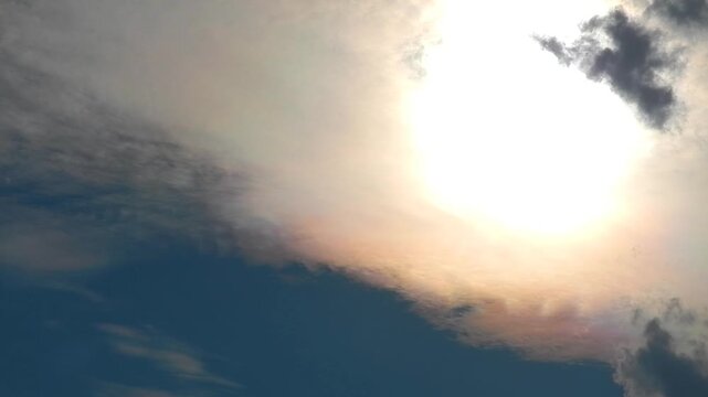 Slowly moving natural clouds texture Altocumulus Duplicatus in blue sky with sun and colorful pearly glow around sunlight. Topics: cloud iridescence, irisation, optical phenomenon, meteorology