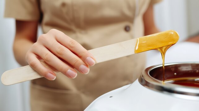 Waxing specialist holding a spatula with warm amber honey wax dripping. Concept of waxing procedure promo.