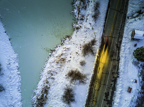 Aerial view of a road cutting through a snow-dusted landscape alongside a turquoise river, a stark contrast of winter's chill and vibrant aquatic hues, Temecula, California, United States.