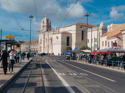 Lisbon, Portugal - 08 November 2025: View of the Jeronimos Monastery's pale stone facade glows under a bright sky, bustling with city life and vibrant commerce.