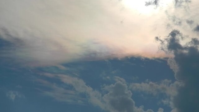 Slowly moving natural clouds texture Altocumulus Duplicatus in blue sky with sun and colorful pearly glow around sunlight. Topics: cloud iridescence, irisation, optical phenomenon, meteorology