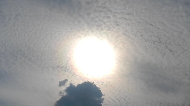 Slowly moving natural clouds texture Altocumulus Duplicatus in sky with sun and colorful pearly glow around sunlight. Topics: cloud iridescence, irisation, optical phenomenon, meteorology, cloud cover