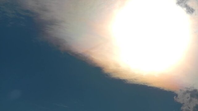 Natural clouds texture Altocumulus Duplicatus in blue sky with sun, colorful pearly glow around sunlight and plane in flight with white streak. Topics: air travel, transport, optical phenomenon
