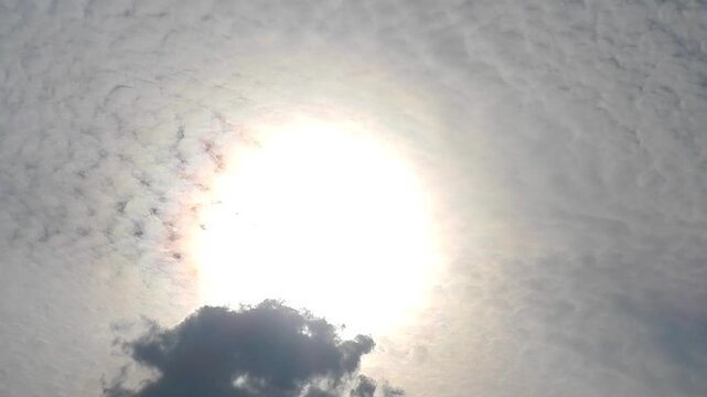Slowly moving natural clouds texture Altocumulus Duplicatus in sky with sun and colorful pearly glow around sunlight. Topics: cloud iridescence, irisation, optical phenomenon, meteorology, weather