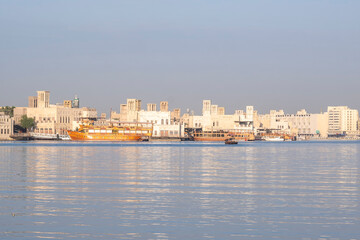 Naklejka premium 12.12.2025 Dubai, UAE. Dubai Creek panoramic view with luxury yachts, traditional wooden dhow boats, and contrast between historic Deira architecture and modern city skyline.