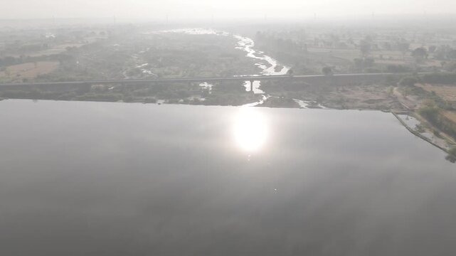 Aerial view of agricultural fields in Bhilwara, Rajasthan during spring harvest, showing half-harvested wheat, crop bundles forming abstract patterns, with the Kothari River flowing through farmland.