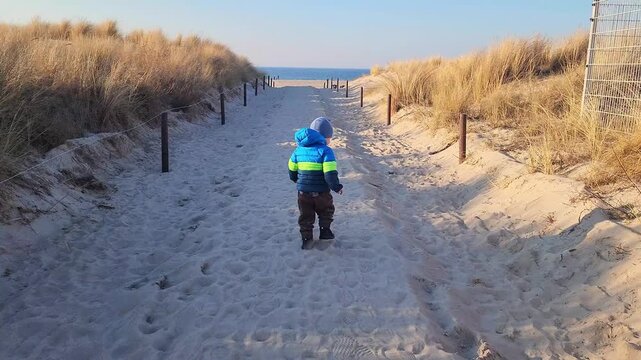 Little boy is running along a sandy path towards the beach