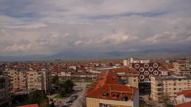 A wide-angle daylight timelapse of Kor&ccedil;&euml;, Albania, showing the urban city center and moving clouds over the surrounding mountain landscape.