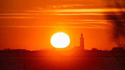 Fototapeta premium Megazoom (600mm) summer sunset or sundowner with a church silhouette seen from near Michaelsbuch, Stephansposching, Deggendorf, Bavaria, Germany