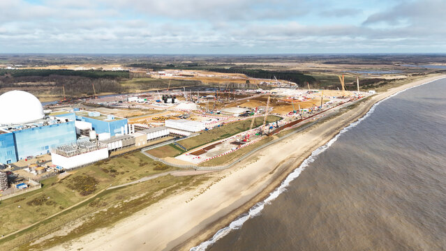 Aerial view of a coastal industrial landscape with a domed structure contrasting against the tan beach and turquoise sea, Sizewell Power Station, Leiston, United Kingdom.