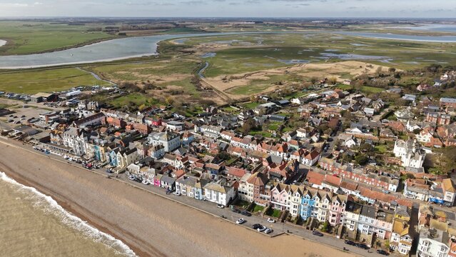 Aerial view of where the North Sea kisses the shingle beach, contrasting with the town's vibrant buildings and the tranquil marshlands beyond, Aldeburgh, England, United Kingdom.