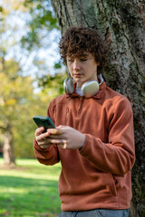 Young man using smartphone while standing against tree in park during daylight © Iryna