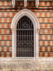 Obraz premium Gothic Arched Window With Decorative Iron Grille and Stone Surround in Patterned Brick Fa?ade