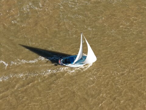 Aerial view of a sailboat sailing on the river with a long shadow cast over the water, Felixstowe ferry port, Felixstowe ferry port, England, United Kingdom.