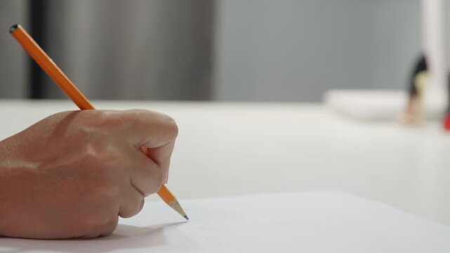Closeup hand writing with pencil on paper, firm grip and quick strokes across white sheet, blurred background suggesting office environment, deadlinedriven energy, focused wrist movement