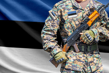 Fototapeta premium Estonia flag with soldier in military uniform holding assault rifle in front of it