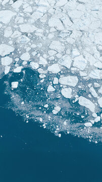 View of ice floes and broken icebergs floating in the deep blue Arctic Ocean in Greenland.