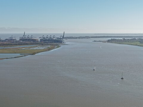 Aerial view of the tranquil, silvery Orwell River meandering towards the North Sea, with distant cranes punctuating the skyline, Felixstowe, United Kingdom.