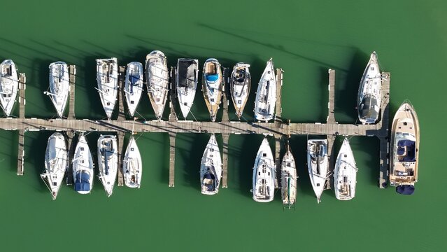 Aerial view of yachts and boats moored along a wooden pier, reflecting in the green water, Suffolk Yacht Harbour, Felixstowe, United Kingdom.