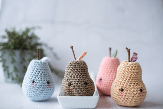 Close-up of four assorted homemade anthropomorphic crochet pear toys (Amigurumi) on a table with a houseplant