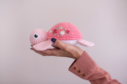 Close-up of a woman's hand holding a homemade pink crochet turtle toy (Amigurumi)