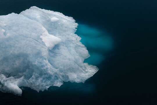 View of a massive iceberg with a glowing turquoise submerged base floating in the dark arctic waters Greenland.