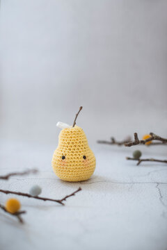 Close-up of a homemade anthropomorphic crochet pear toy (Amigurumi) on a table surrounded by branches