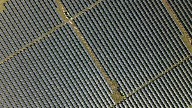 Aerial view of geometric solar panels gleaming under the sun, contrasting with the surrounding grassy patches, Felixstowe, United Kingdom.