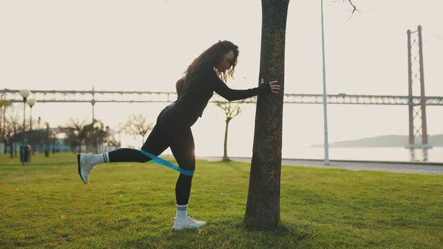 Athletic woman exercising glutes with resistance band in park